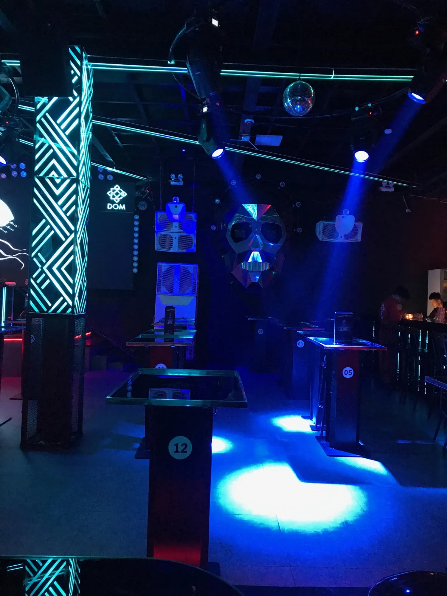 Không gian bên trong Dom Club sau khi hoàn tất thi công, với biểu tượng thương hiệu DOM, mặt nạ trang trí sân khấu và các bàn VIP đánh số.