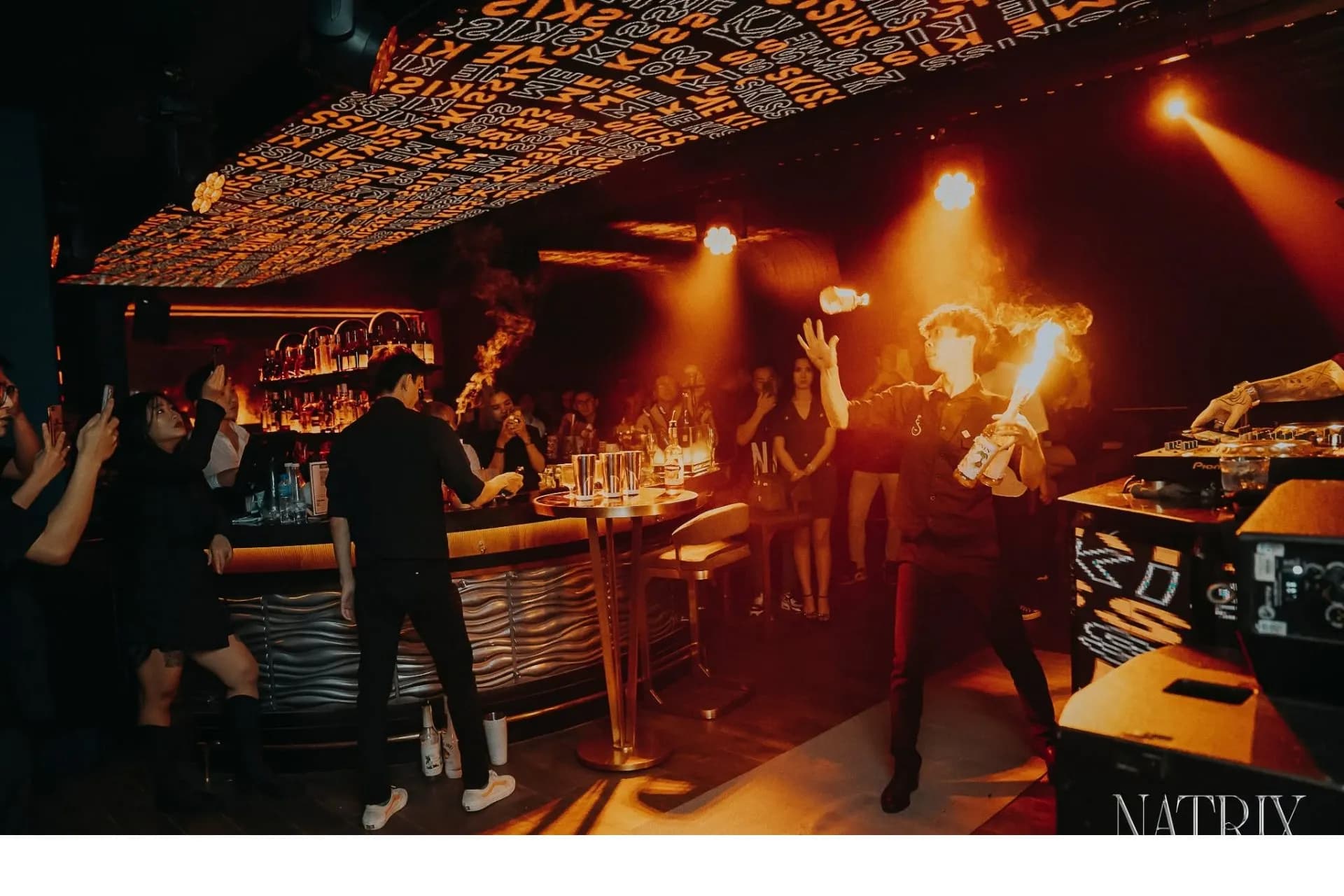 Nhân viên biểu diễn lửa (Flair Bartending) tại quầy bar trung tâm Natrix, không gian đông khách về đêm.