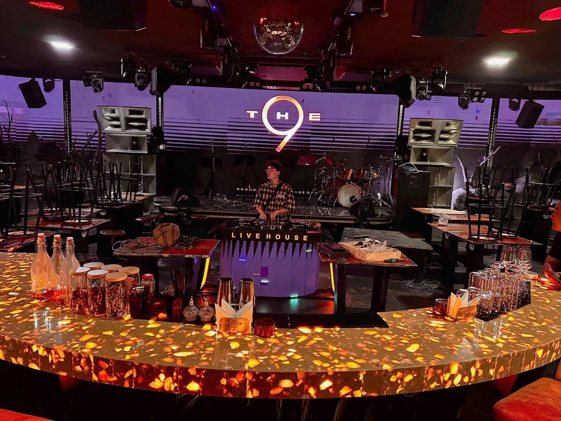Sân khấu và quầy bar trung tâm tại The9 BH Live House, với biển hiệu thương hiệu THE9 và bục DJ LIVE HOUSE, sau khi hoàn tất thi công.