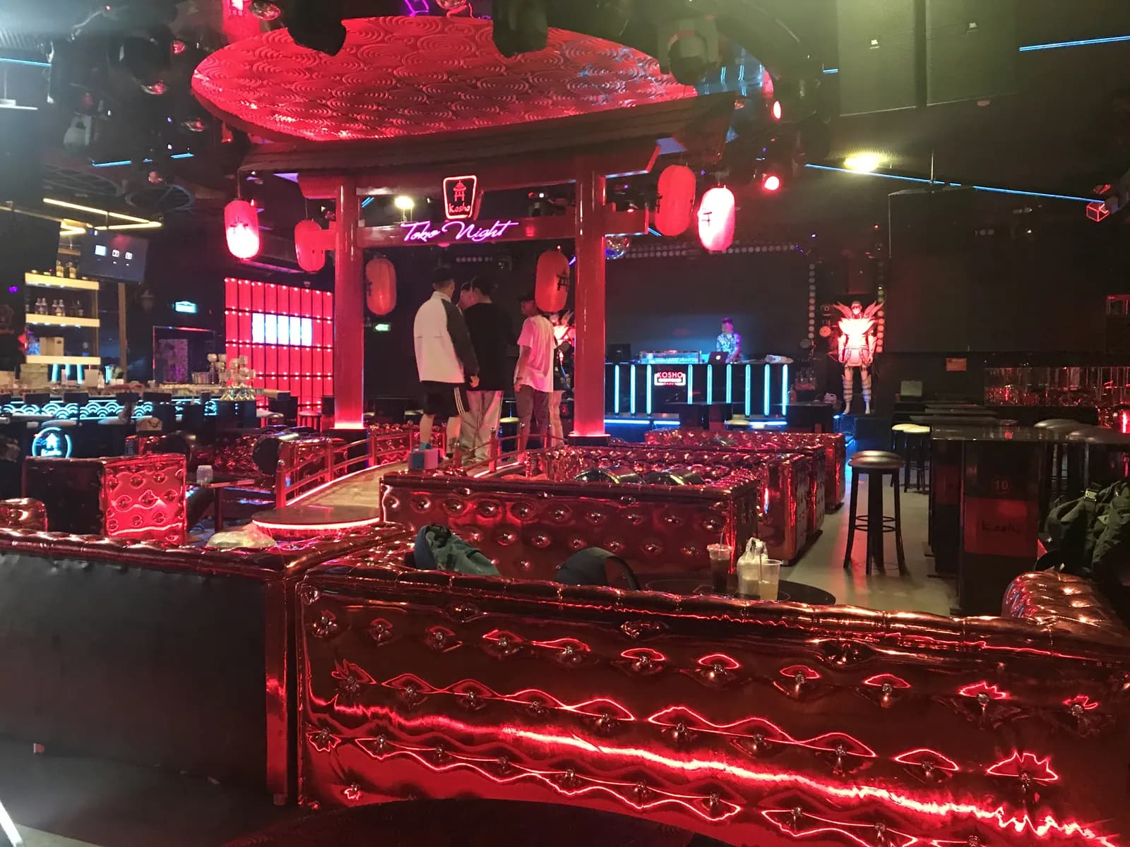 Không gian club Kosho nhìn từ lối vào dạng cổng torii sơn đỏ, ánh sáng đỏ và xanh, khu DJ phía xa và các băng ghế bọc kim loại đỏ hai bên.