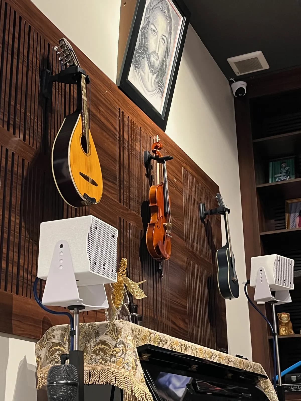 Một cặp loa treo tường lắp đặt ngay dưới góc trưng bày đàn mandolin, violin và guitar trên vách gỗ tại nhà riêng.