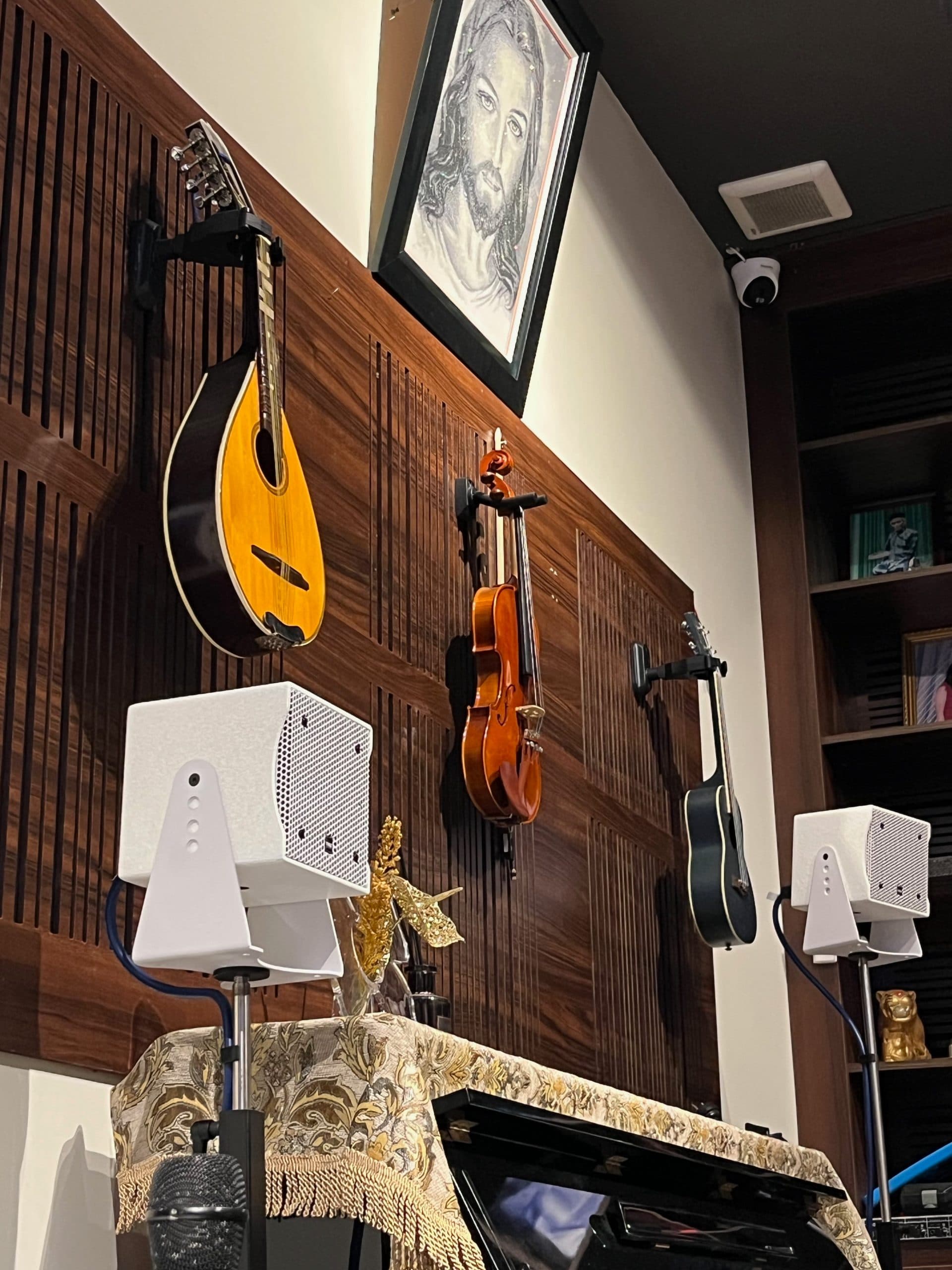Một cặp loa treo tường lắp đặt ngay dưới góc trưng bày đàn mandolin, violin và guitar trên vách gỗ tại nhà riêng.